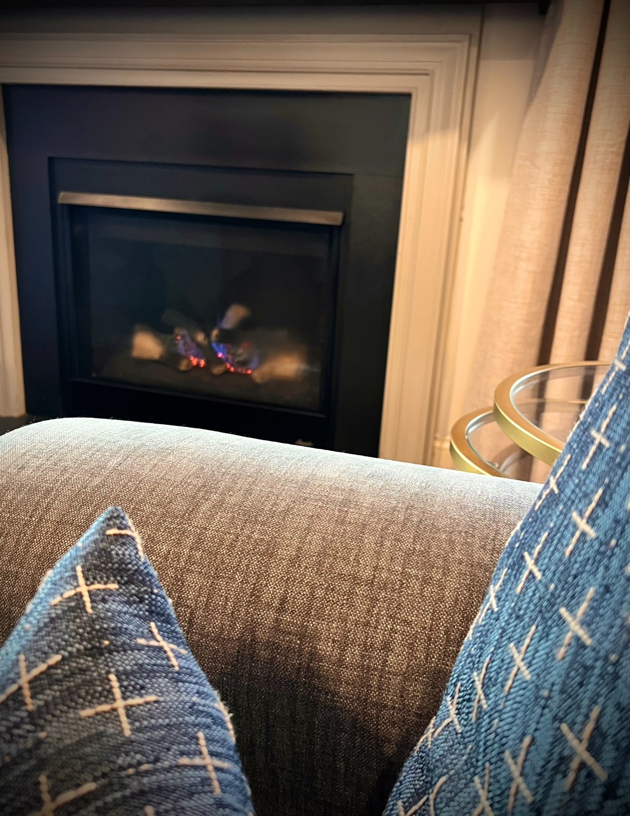 Warm fireplace vignette with patterned pillows and a glass table