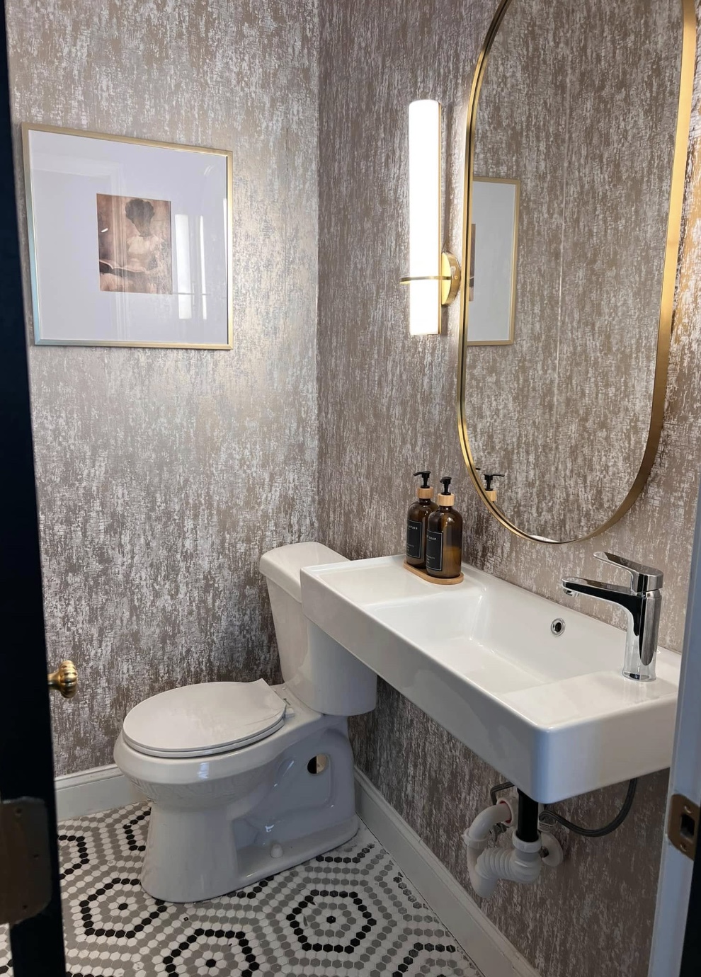 Atlanta powder room with metallic wallpaper, sculptural lighting, and brass-framed mirror